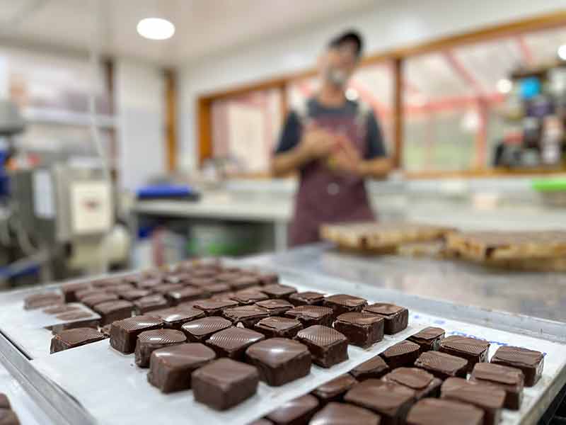 Homem explica detalhes da fabricação do chocolate com bombons à frente na Chocolaterie, no Circuito Chico, em Bariloche