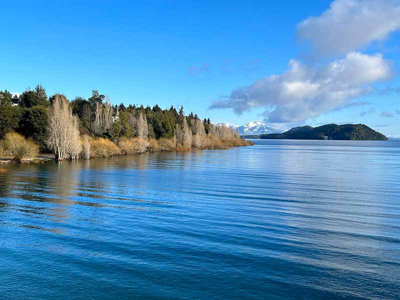 Playa Bonita e lago com montanha com neve ao fundo em dia de céu azul no Circuito Chico em Bariloche