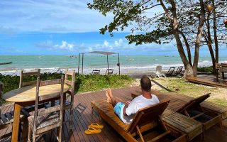 Homem sentado em frente à praia na Areia Preta, uma das pousadas em Cumuruxatiba, na Bahia