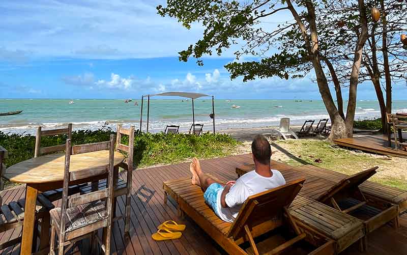 Homem sentado em frente à praia na Areia Preta, uma das pousadas em Cumuruxatiba, na Bahia