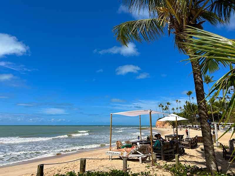 Pessoas na areia da Barra do Cahy em dia de sol e céu azul