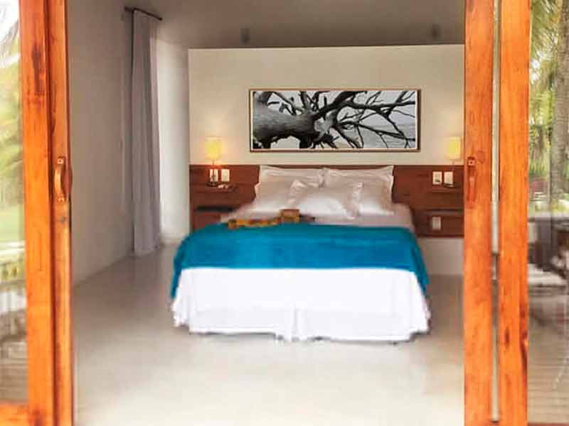 Quarto da Vila Bela Vista, dica entre as pousadas em Corumbau, com cama de casal, quadro e grande porta de vidro