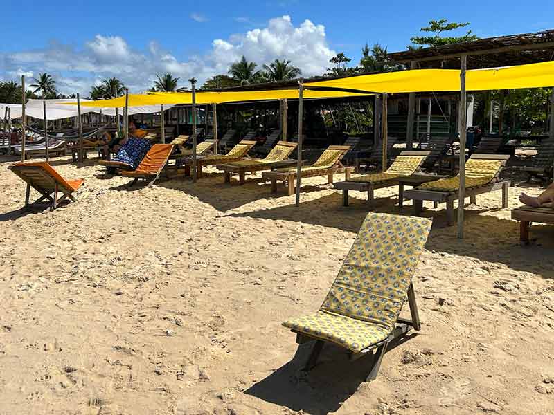 Cadeiras de praia e toldo amarela no Cantinho Nativo, na Bahia