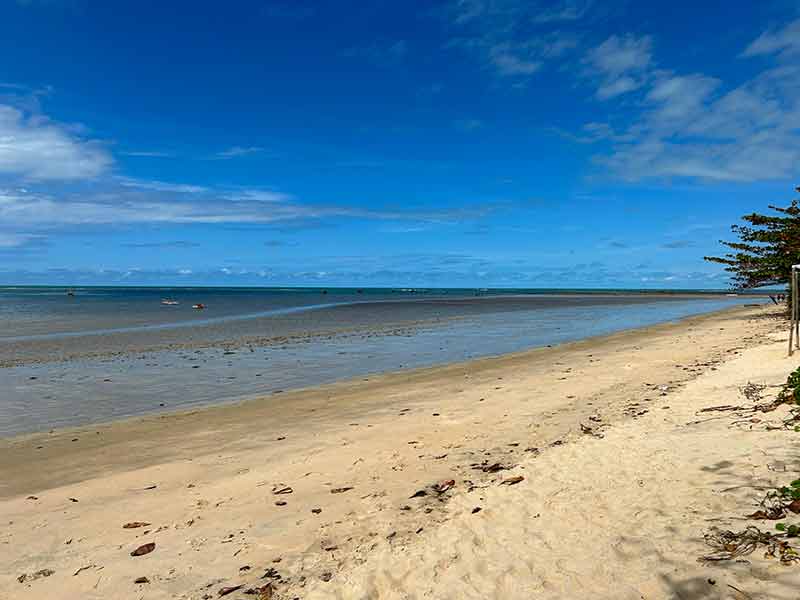 Areia e mar vazios da praia da vila de Cumuru, na Bahia, em dia de céu azul