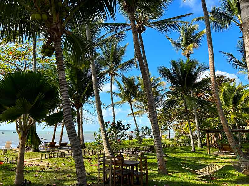 Área externa da pousada Areia Preta, em Cumuruxatiba, com mesas no jardim em frente à praia