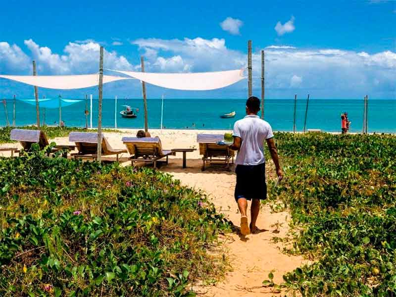 Garçom indo servir hóspede na área de praia da Loin de Tout, dica de pousada na Ponta do Corumbau