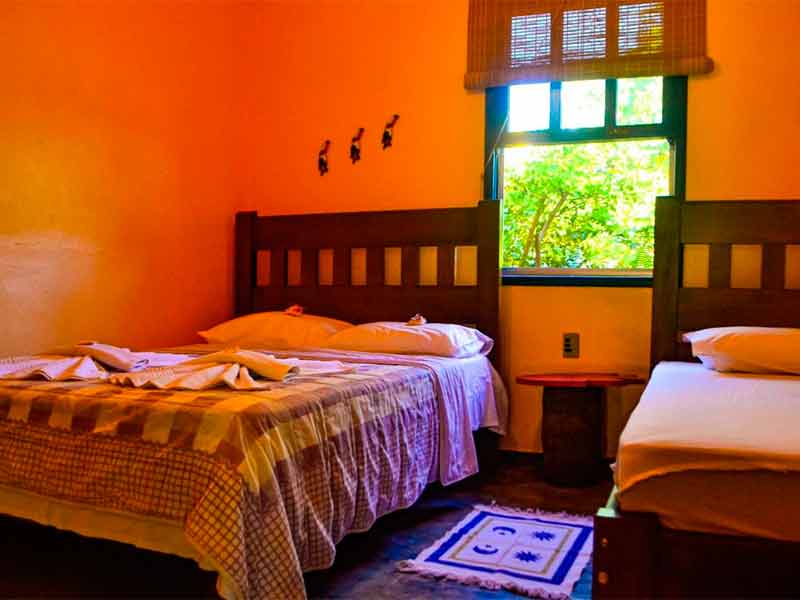 Quarto da Pousada das Cores com duas camas, janela e parede laranja