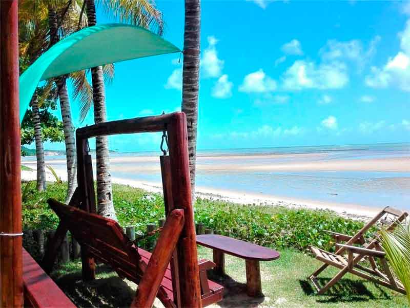 Área externa da Pousada das Cores, dica de onde ficar em Cumuruxatiba, com cadeiras em grama em frente à praia