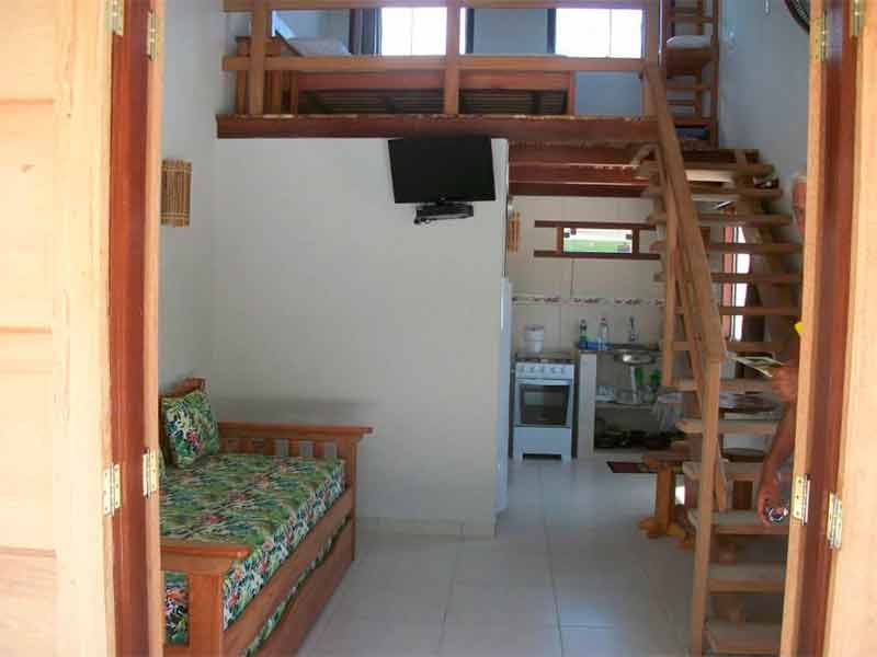 Chalé da Vila Guaiamum com sofá, cozinha com fogão, TV e escada
