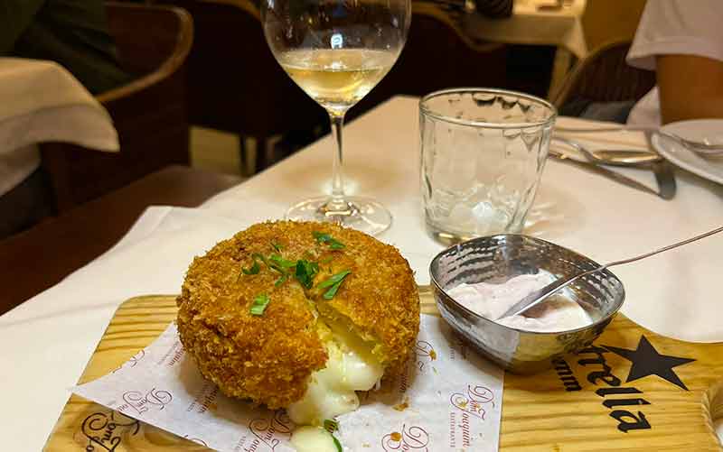 Queijo de ovelha empanado derretendo com vinho ao fundo no Dom Joaquim