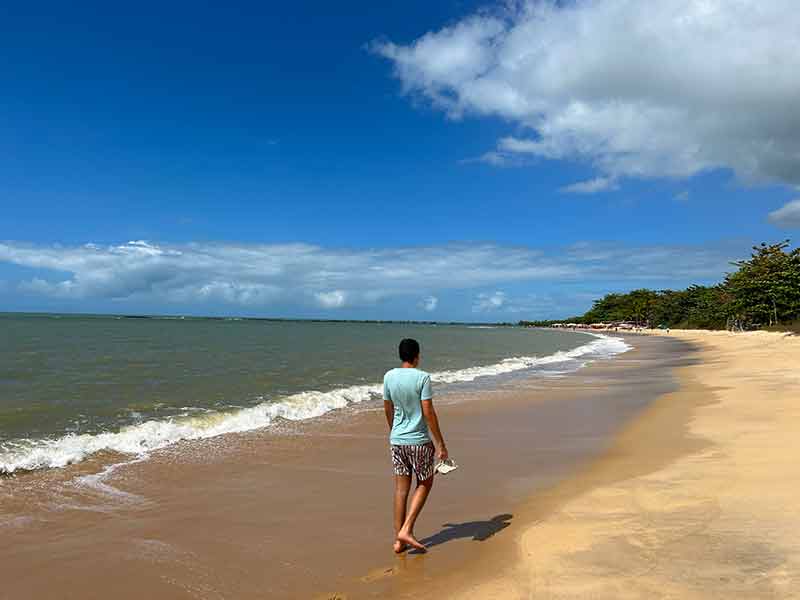 Homem caminha pelas areias vazias da praia de Santo André na Bahia em dia de céu azul