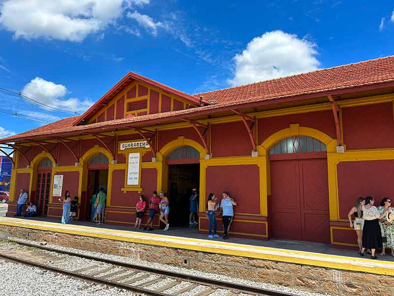 Estação de trem de Guararema com pessoas na sombra em dia de céu azul com algumas nuvens