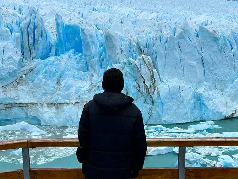 Homem parado observa a grandiosidade do Perito Moreno em seus tons azuis e brancos