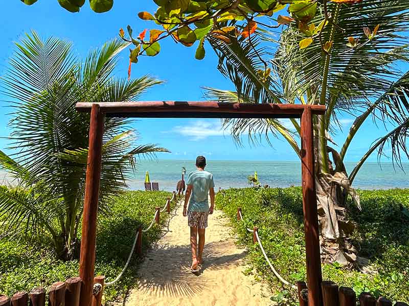 Homem caminha rumo à praia de Santo André na Bahia em dia de céu azul