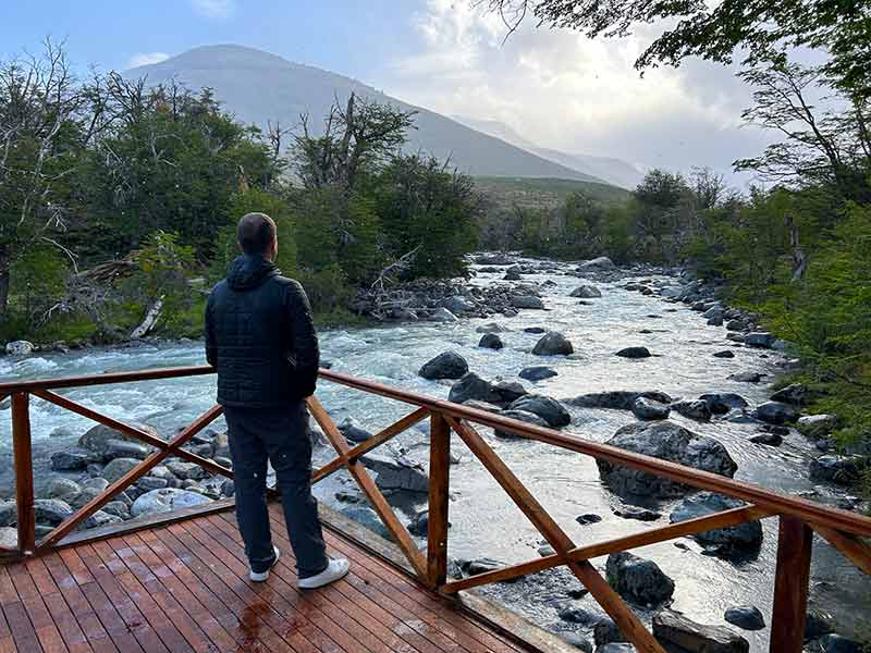 Homem parado observa lago com montanha ao fundo na estância Tierras Patagoicas, em El Calafate