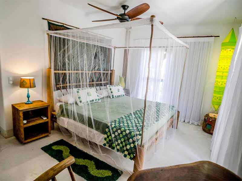Quarto da Udêxerê com cama de casal, mosquiteiro, tapete, abajur e ventilador de teto