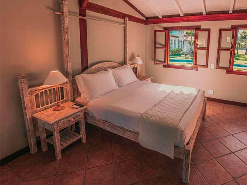 Quarto do Vila Angatu com cama de casal, abajur e duas janelas
