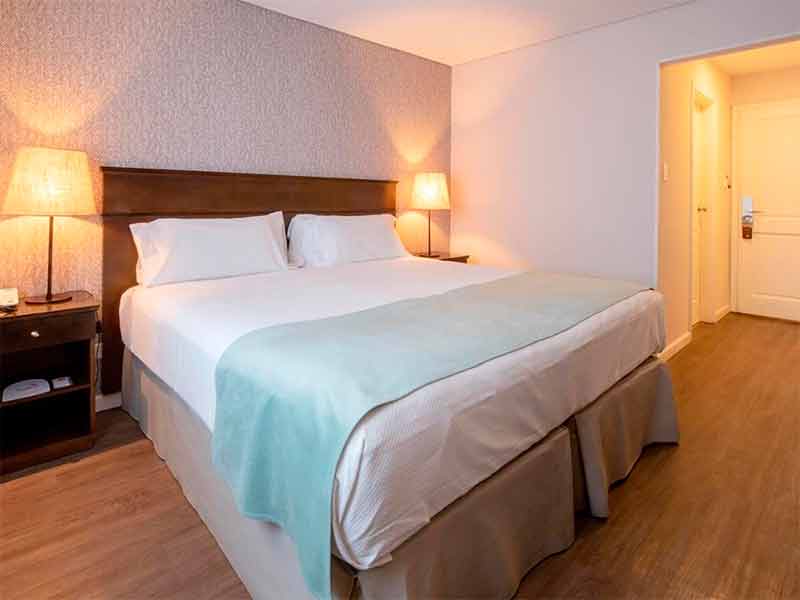 Quarto do Calafate Parque Hotel com cama de casal, abajur e piso de madeira