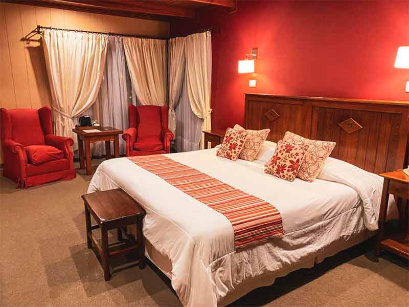 Quarto do La Cantera com cama de casal, paredes vermelhas e duas poltronas