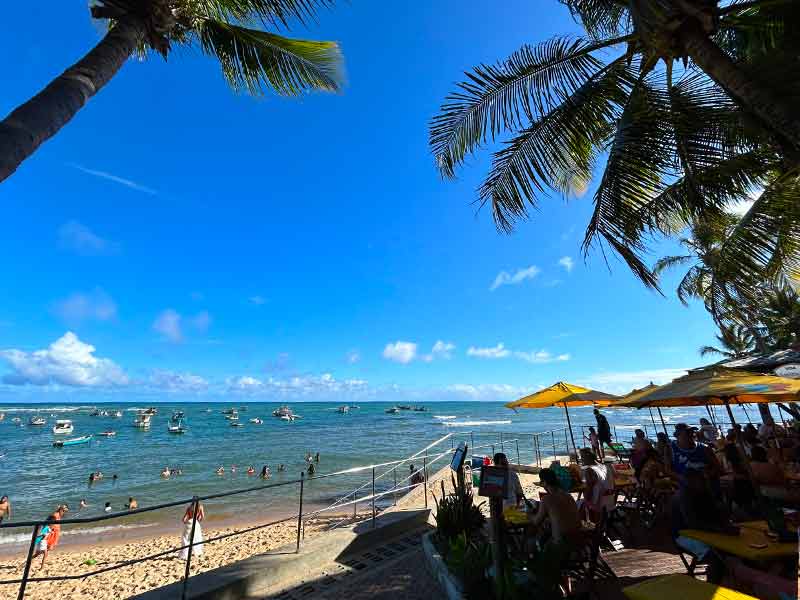 Pessoas nadam no mar da praia do Portinho, dica de o que fazer na Praia do Forte, com bar na orla