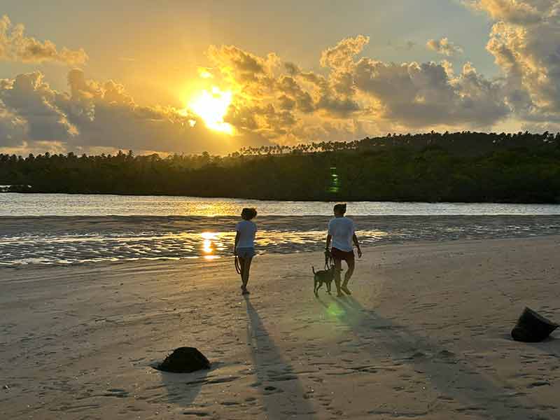 Pessoas caminham no pôr-do-sol na Boca do Rio Tatuamunha em Porto de Pedras
