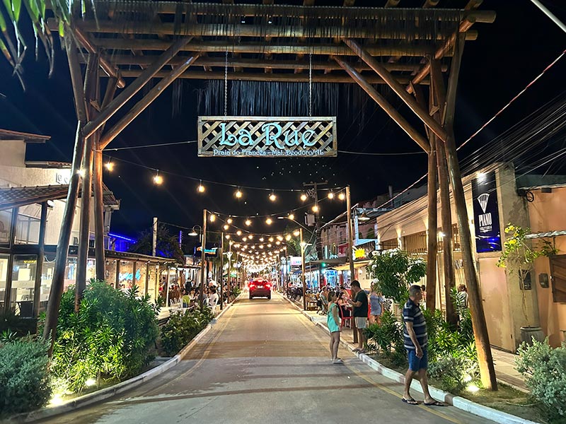 Pessoas no portal da La Rue, rua da Praia do Francês, com restaurantes e bares