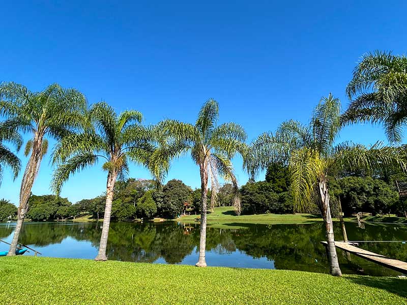 Árvores, gramado e lago em dia de céu azul no Areia que Canta