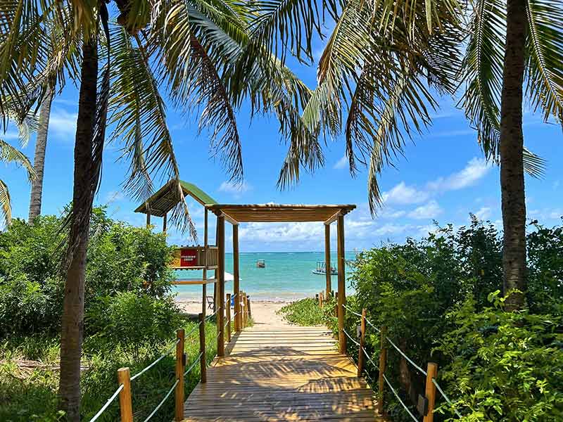 Passarela dá acesso à Praia do Patacho com mar calmo e céu azul