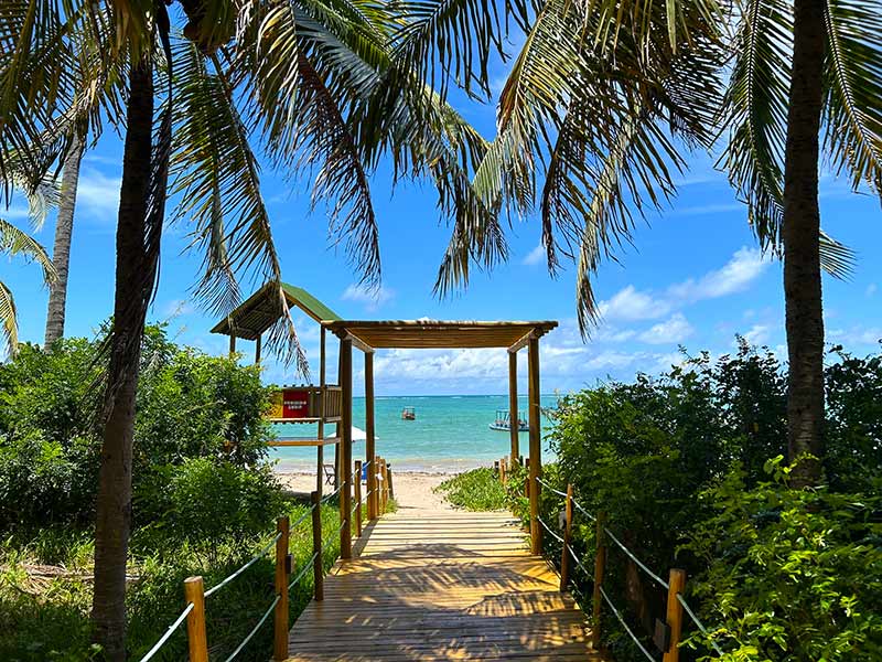 Caminho pra Praia do Patacho com mar esverdeado em dia de céu azul