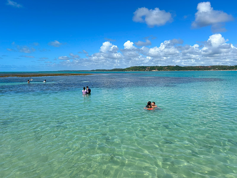 Pessoas nadam nas águas claras das Piscinas naturais de Japaratinga