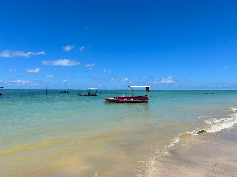 Barco parada em mar esverdeado da Praia do Toque, em Alagoas