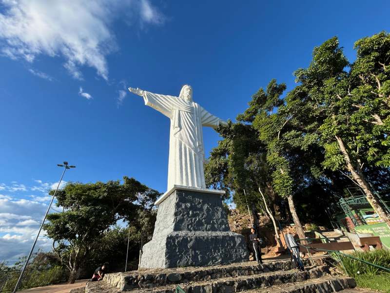 Cristo Redentor, de Serra Negra, em dia de céu azul. com árvores ao lado