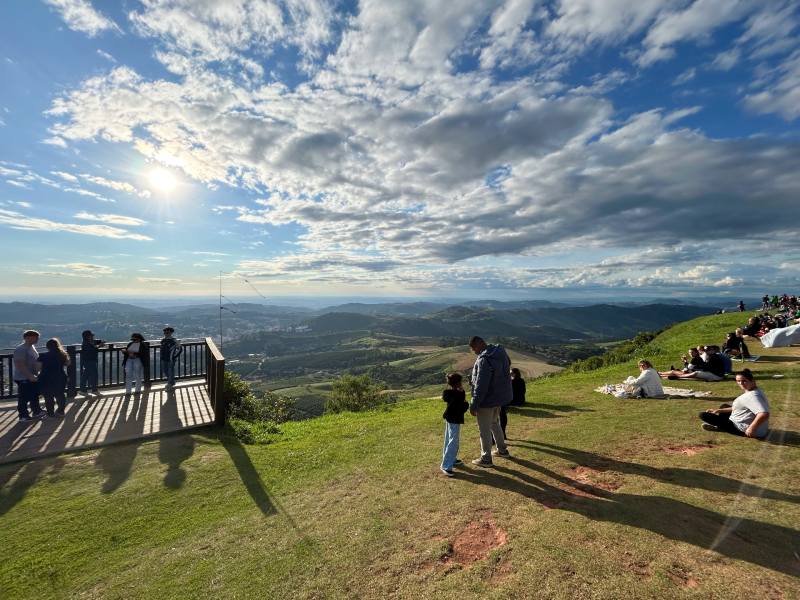 Pessoas no gramado e no deck curtem pôr do sol no Mirante Alto da Serra, dica de o que fazer em Serra Negra