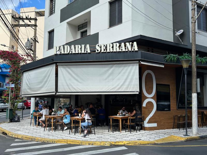 Pessoas sentadas na calçada almoçam na Padaria Serrana, dica de onde comer em Serra Negra