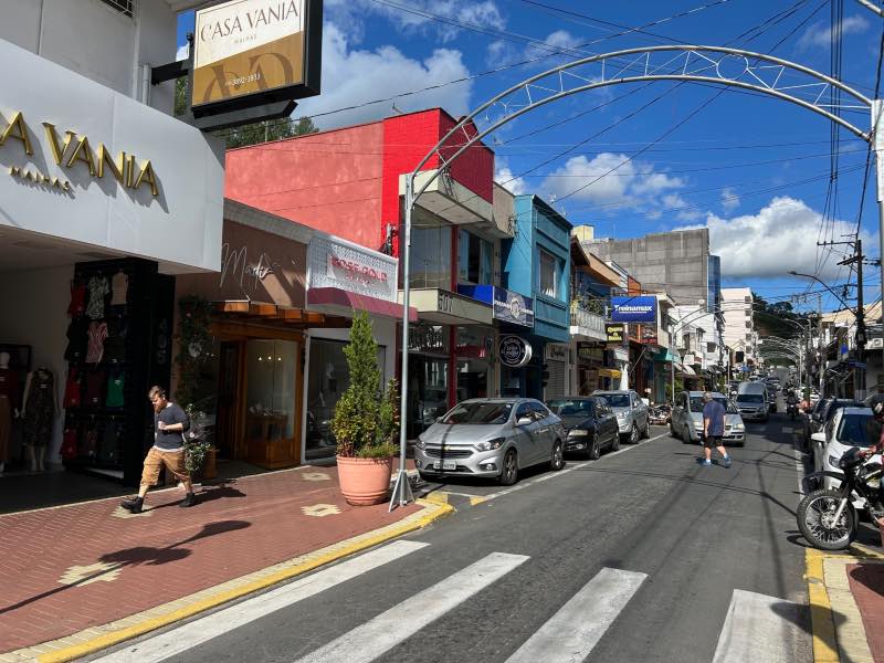 Rua de comércio em Serra Negra com pessoas e carros em dia de céu azul com nuvens