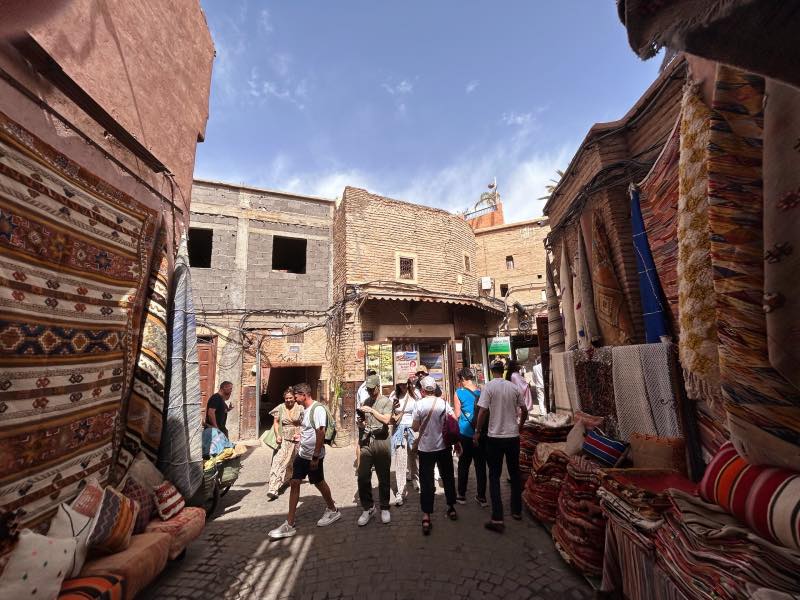 Pessoas caminham entre os souks na Medina em dia de céu azul, dica de o que fazer em Marrakech