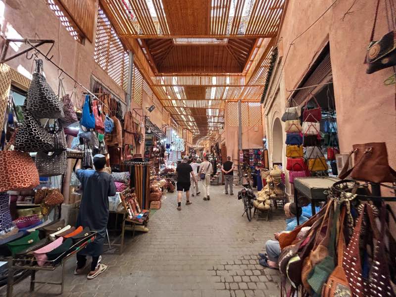Pessoas andando em um souk na Medina com bolsas penduradas, dica de o que fazer em Marrakech