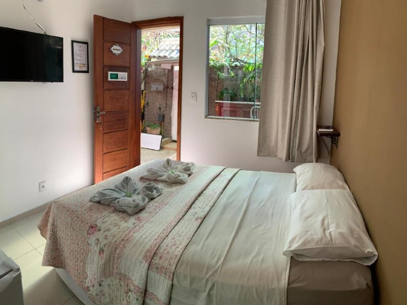 Quarto da Bougainville Suítes com cama de casal, TV e porta aberta