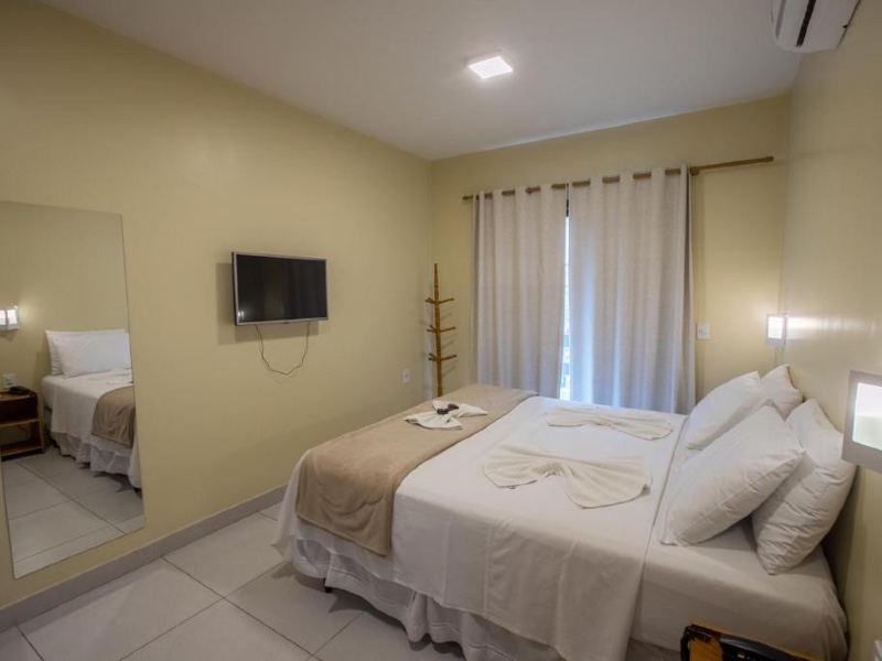 Quarto da pousada Costa Dourada, dica de onde ficar em Arraial do Cabo, com cama de casal, cortina branca e paredes amarelas