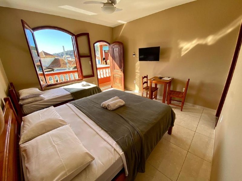 Quarto da Paraíso dos Corais, dica de pousada em Arraial do Cabo, com camas de casal e de solteiro, TV e mesa