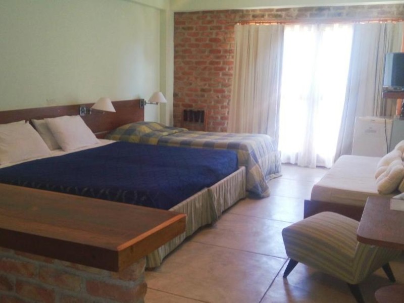Quarto da Pousada Pilar com cama de casal e de solteiro e parede de tijolos