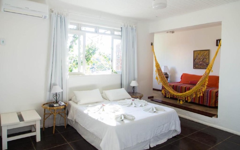 Quarto do Hotel Praia dos Anjos com cama de casal, rede, e decoração branca