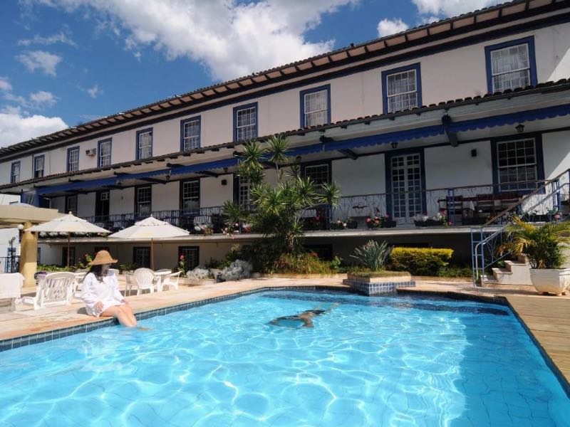 Área da piscina com mulher sentada e pessoa nadando na Pousada do Garimpo