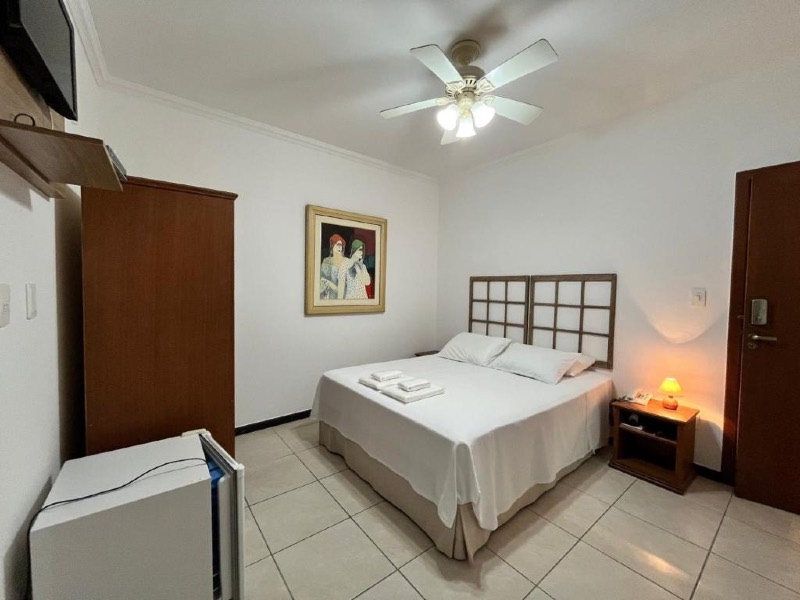 Quarto da Vila do Imperador com cama de casal, abajur e parede branca