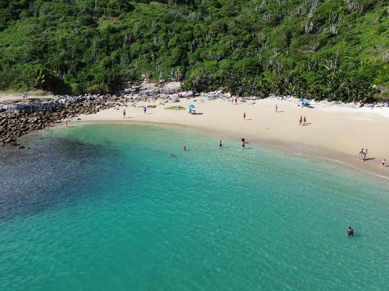 Pessoas no mar esverdeado e nas areias da Praia das Conchas