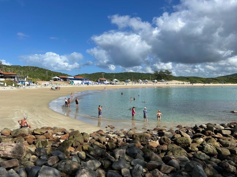Pessoas aproveitam a Praia das Conchas, dica de o que fazer em Cabo Frio, em dia de céu azul com nuvens