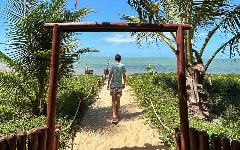 Homem caminha rumo ao mar em Santo André, uma das praias do sul da Bahia, em dia de céu azul