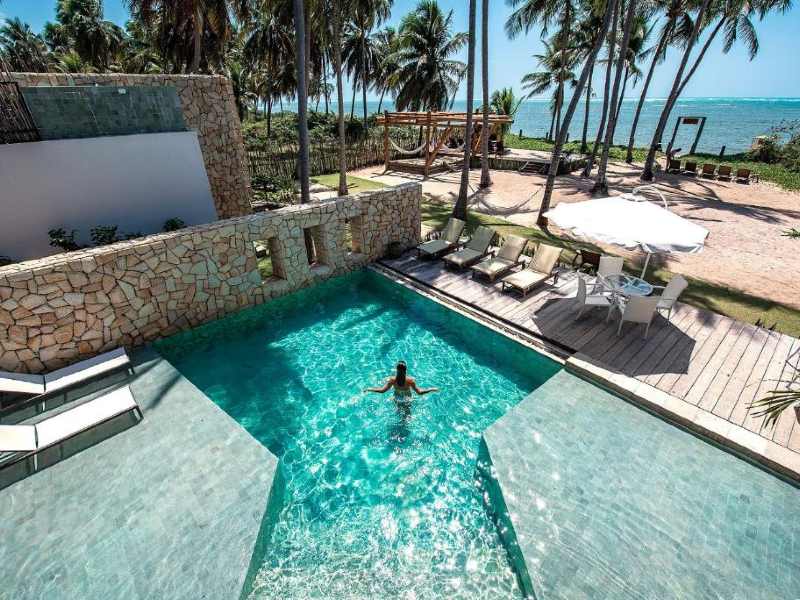 Mulher em pé em piscina na Pedras do Patacho, uma das pousadas na Praia do Patacho, em frente à praia em dia de sol