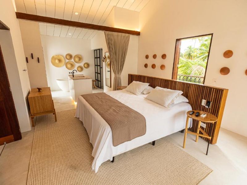 Quarto da Villa Canziani & Donato com cama de casal, banheira ao fundo e chapéus de decoração na parede