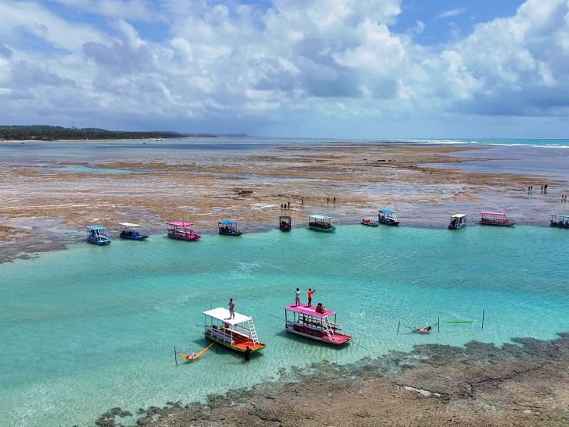 Barquinhos parados nas Piscinas Naturais do Patacho com água esverdeado e céu azul com nuvens